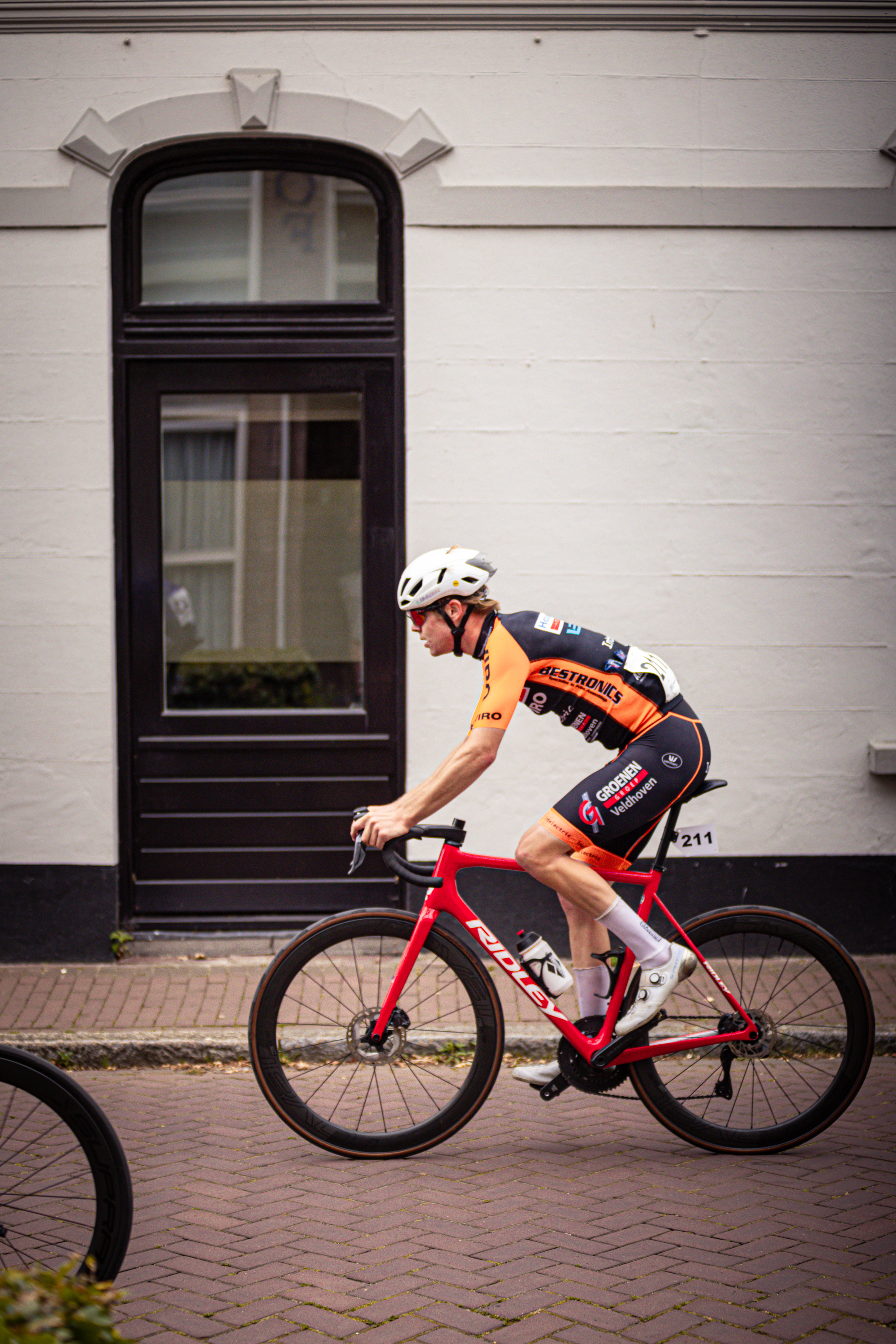 A bicyclist is riding a red and black bike on a brick street.