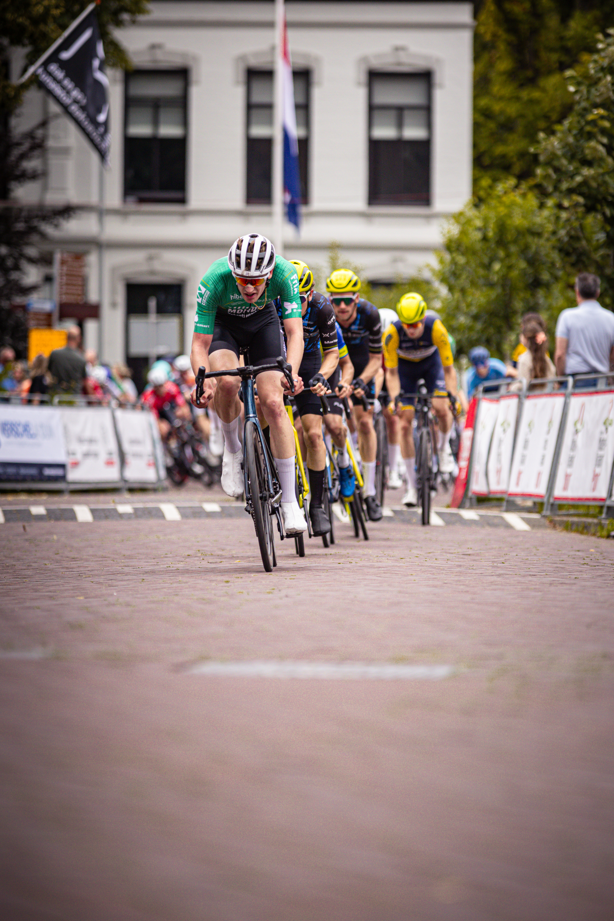 Four cyclists on a track with one wearing a green shirt and white helmet.