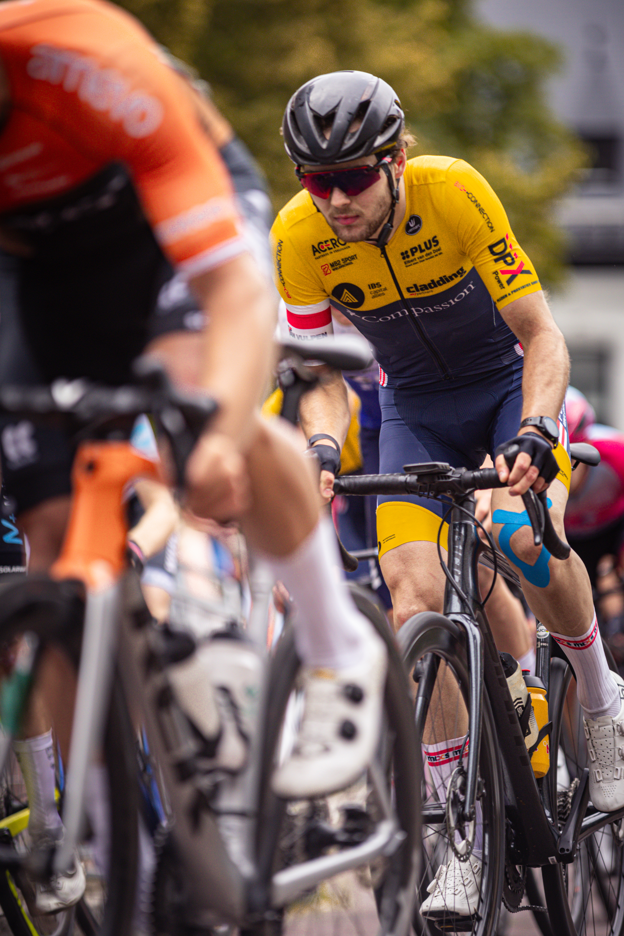 A cyclist in a yellow jersey rides a black bike on the road.