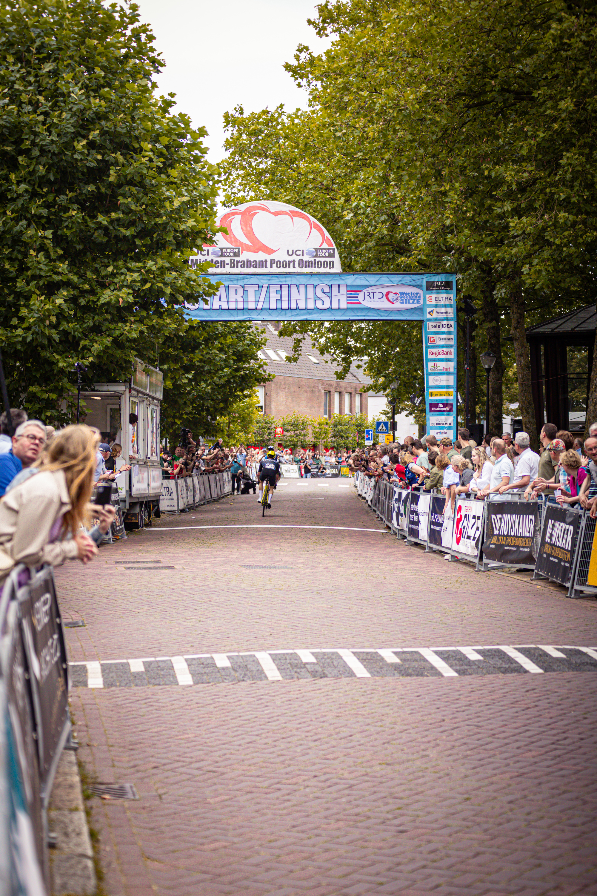A picture of a crowd watching a cyclist on a track with the text "Wielrennen" above it.