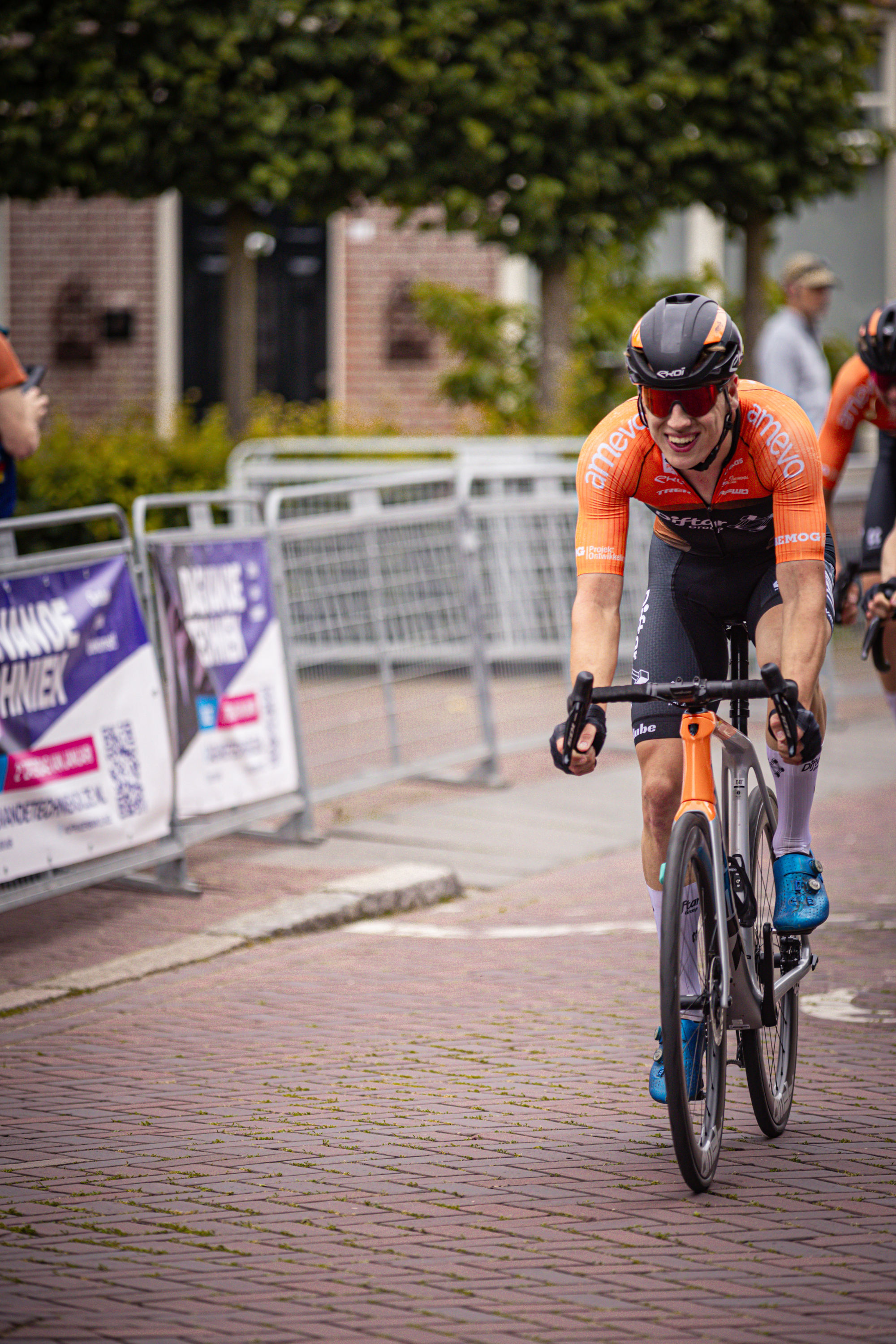 A man in an orange shirt is riding a bike on a brick road.