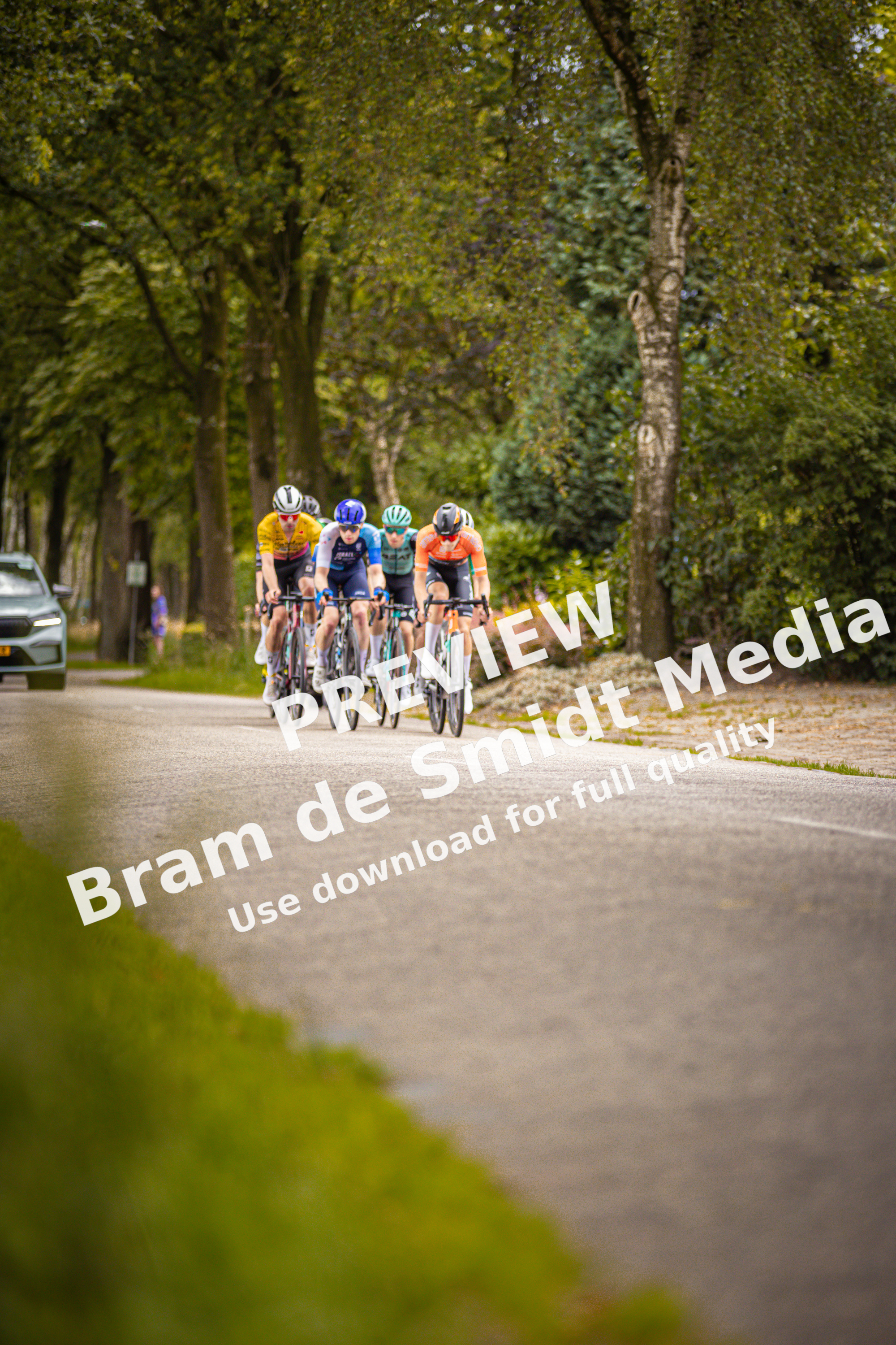 Four cyclists ride down a road in Midden Brabant, participating in the Poort Omloop race.