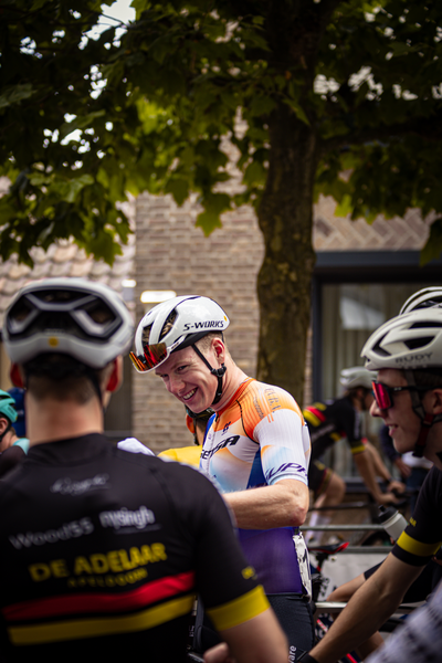 Two men wearing helmets and orange shirts are sitting on their bikes.