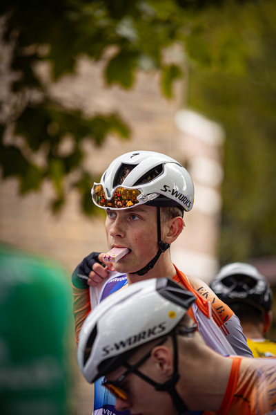 A man eating a donut while riding his bike in the "Midden Brabant Poort Omloop".