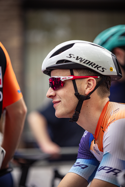 A man wears a black and white helmet with the name S-Works on it. He also has orange glasses on his face.