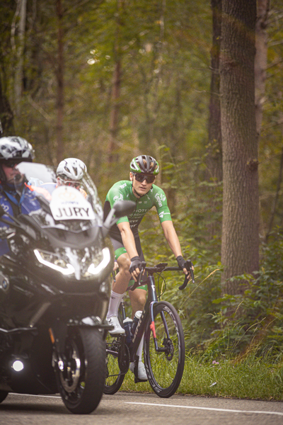 Three cyclists riding on a road with the man in green on the left saying Wielrennen Midden Brabant Poort Omloop.