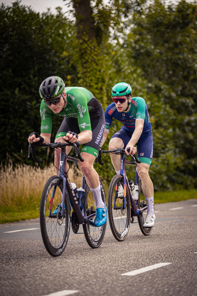 Two cyclists wearing matching helmets are riding in a race on a road.