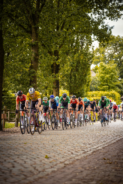 A group of cyclists race down a cobblestone street in the Midden Brabant Poort Omloop.