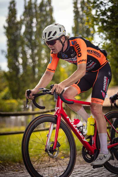 A cyclist in an orange shirt and helmet riding a red bike.