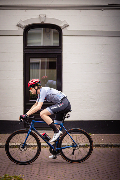 A man on a blue bicycle wearing a red helmet is riding past a white building.