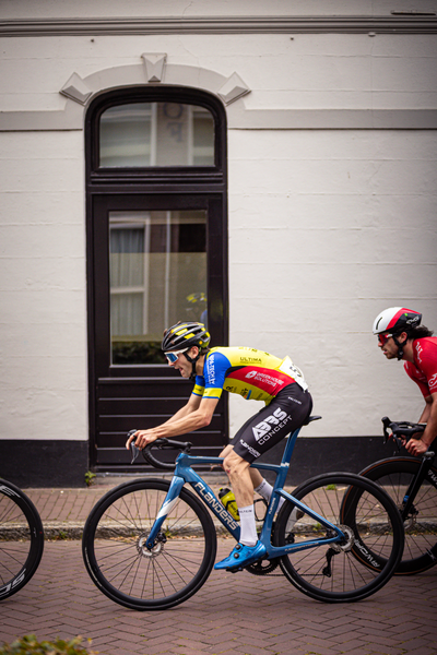 Two cyclists wearing colorful jerseys and a bicycle with the word "wielrennen" on it.