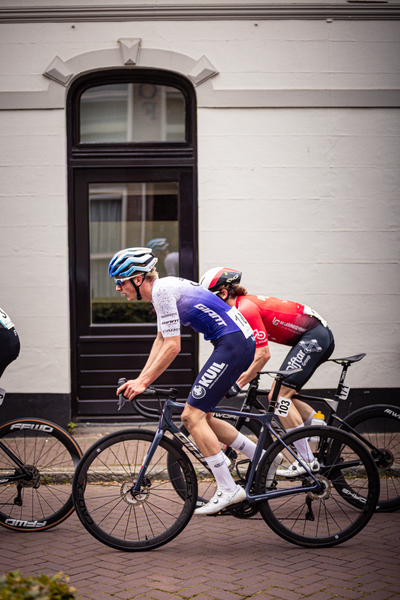 Three cyclists in a line up on a brick road, with one man leading wearing a white and blue jersey that says "Giacomo" on it.