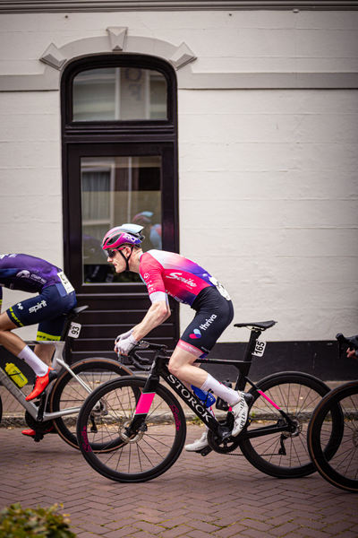 Two cyclists race down a road, one of them wearing a pink and purple jersey with the number 5 on it.