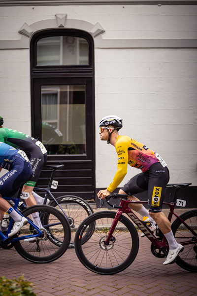 A man is riding a bicycle in a yellow and black shirt during the Midden Brabant Poort Omloop.