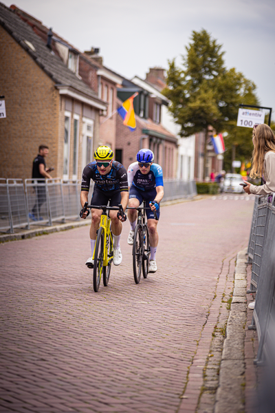 A couple of men are cycling down a street in Midden Brabant Poort Omloop.