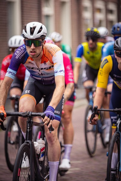 A man is wearing a purple and orange shirt as he rides on a bicycle.