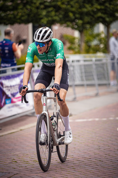 A man is riding a bike down a road with a crowd watching. The man is wearing a helmet and a jersey that says "Wielrennen".