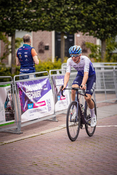 A man in a white jersey is racing on his bicycle near some banners.