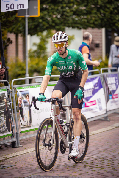 A man wearing a green jersey is riding a bike with the words "Midden Brabant Poort Omloop" written on it.