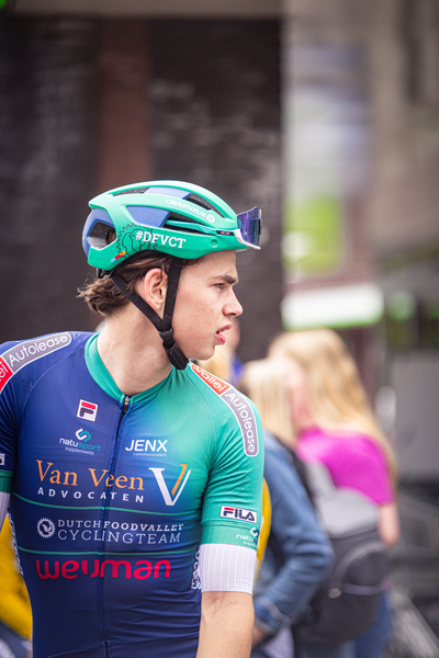 A man wearing a blue and green cycling suit is wearing a Van Veen helmet.