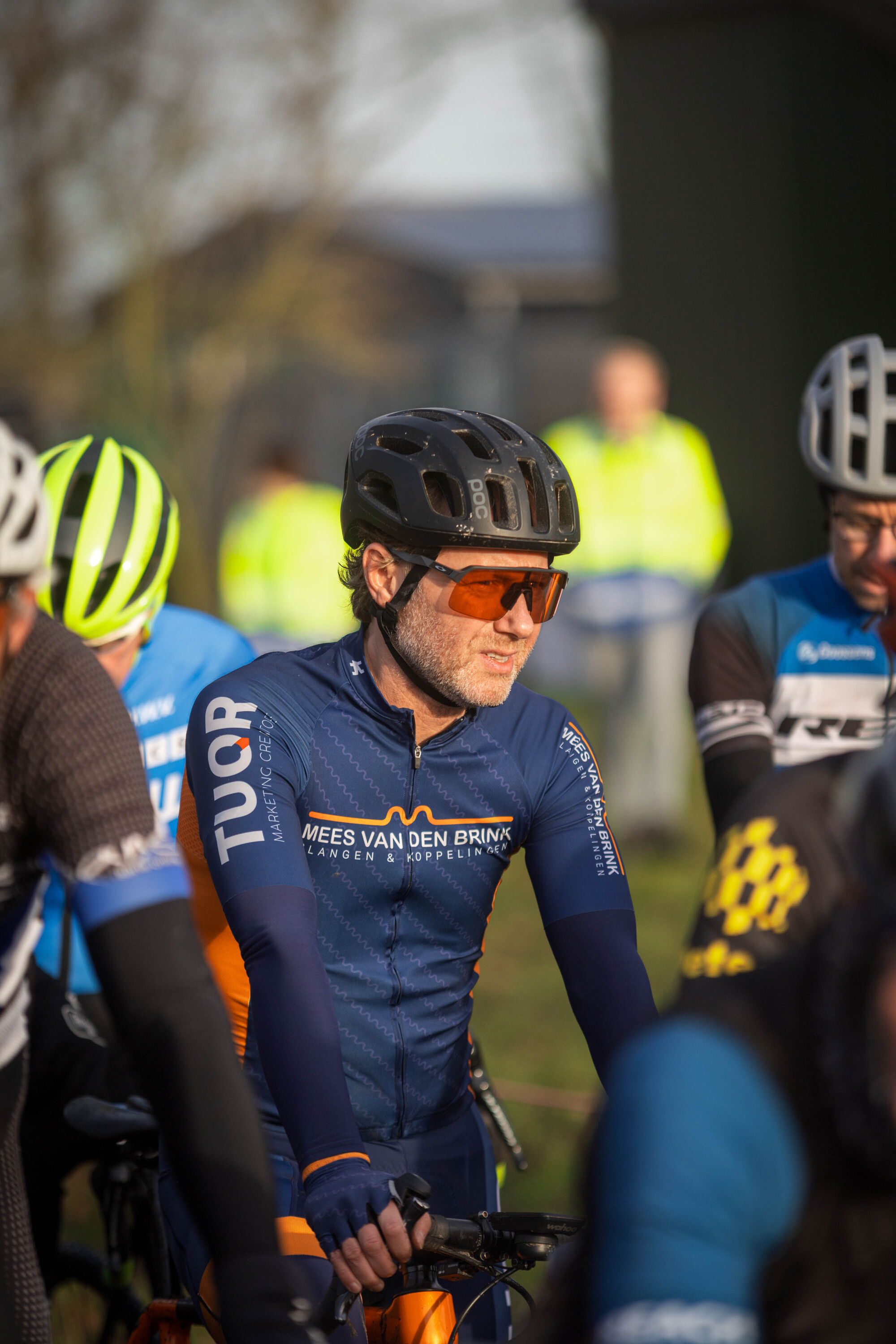 A man in a blue and orange Masters Cycling Club jersey is wearing a black helmet.