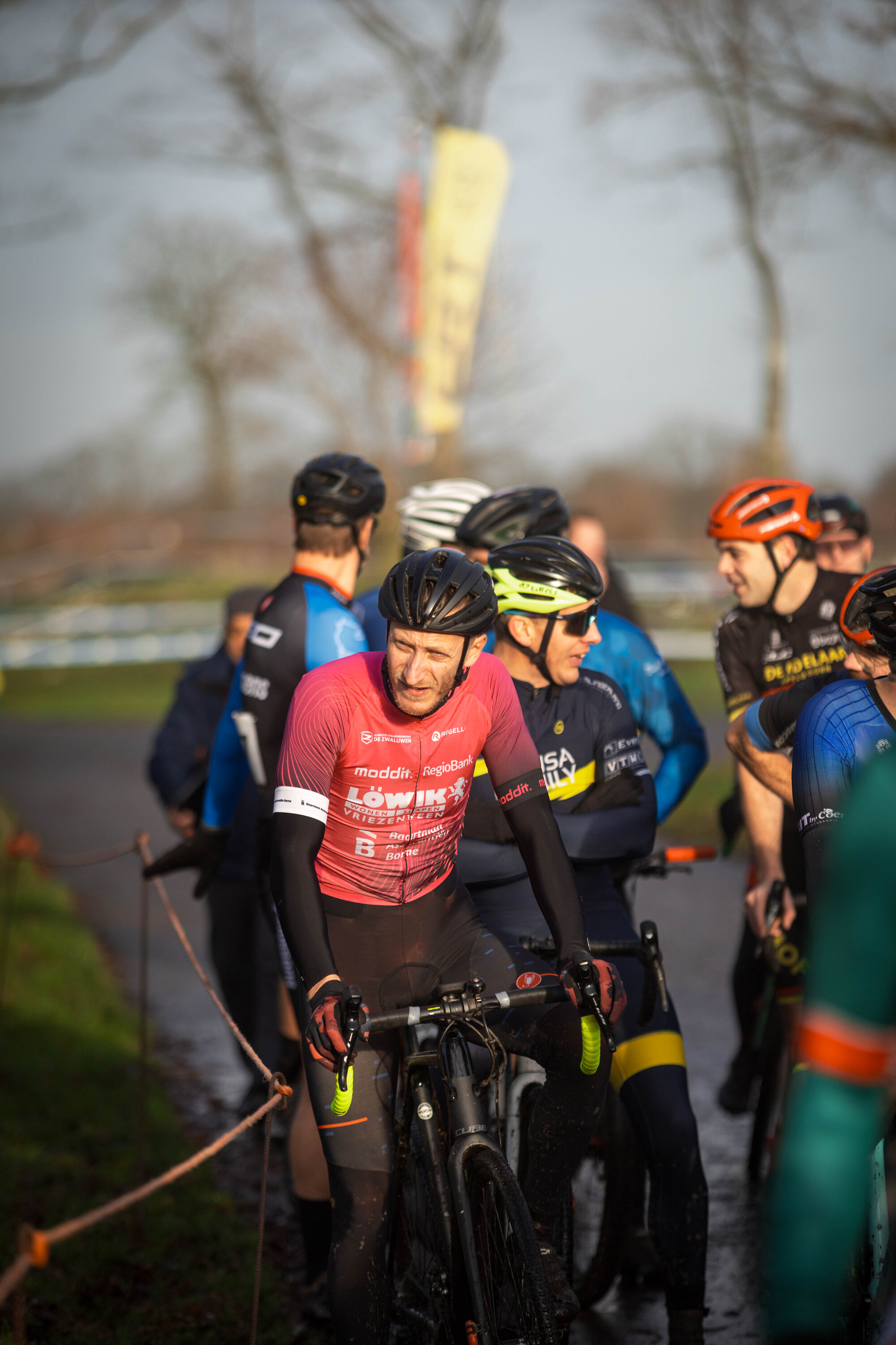 Several people with their bikes gathered in a grassy area, some wearing red and blue shirts.