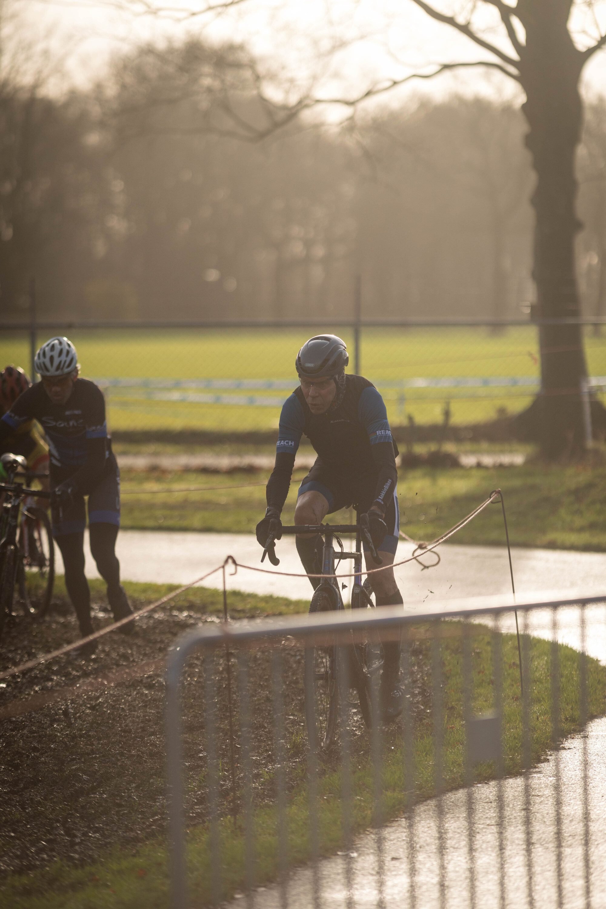 Two cyclists, one wearing a blue shirt, race each other on a track.