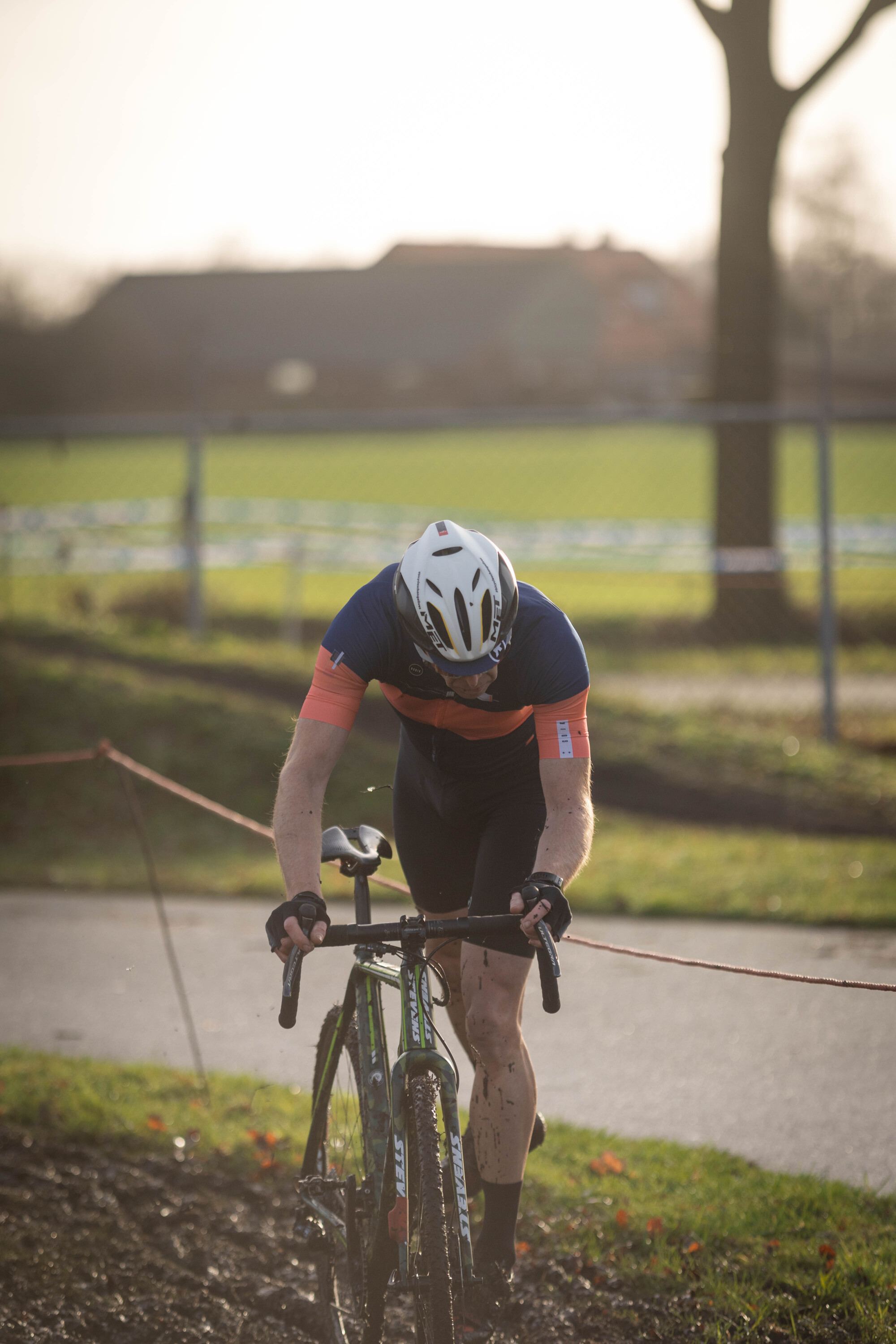 A man in a blue and orange shirt riding a black and white bicycle. He is wearing a helmet with a number 1 on it.