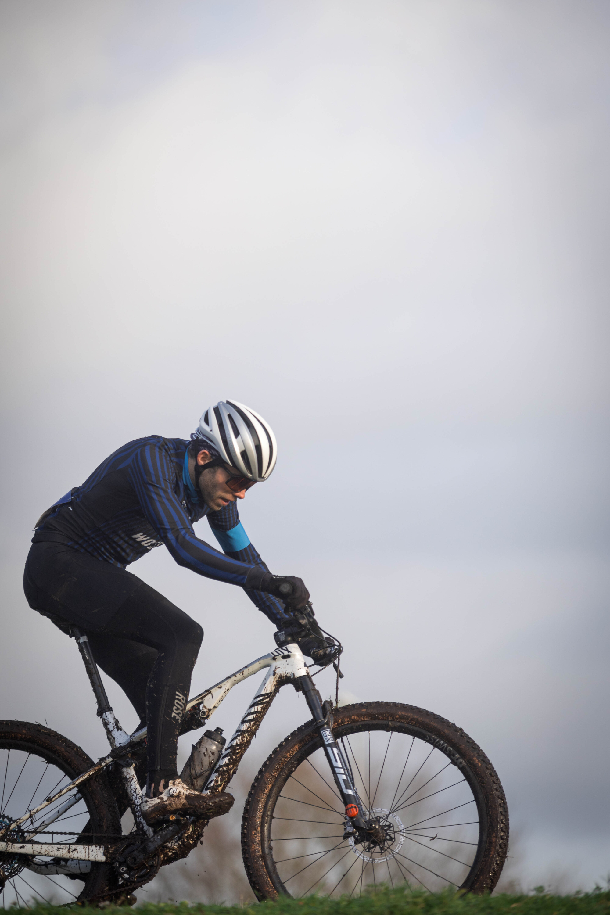 A man is riding a white and blue mountain bike in the rain.