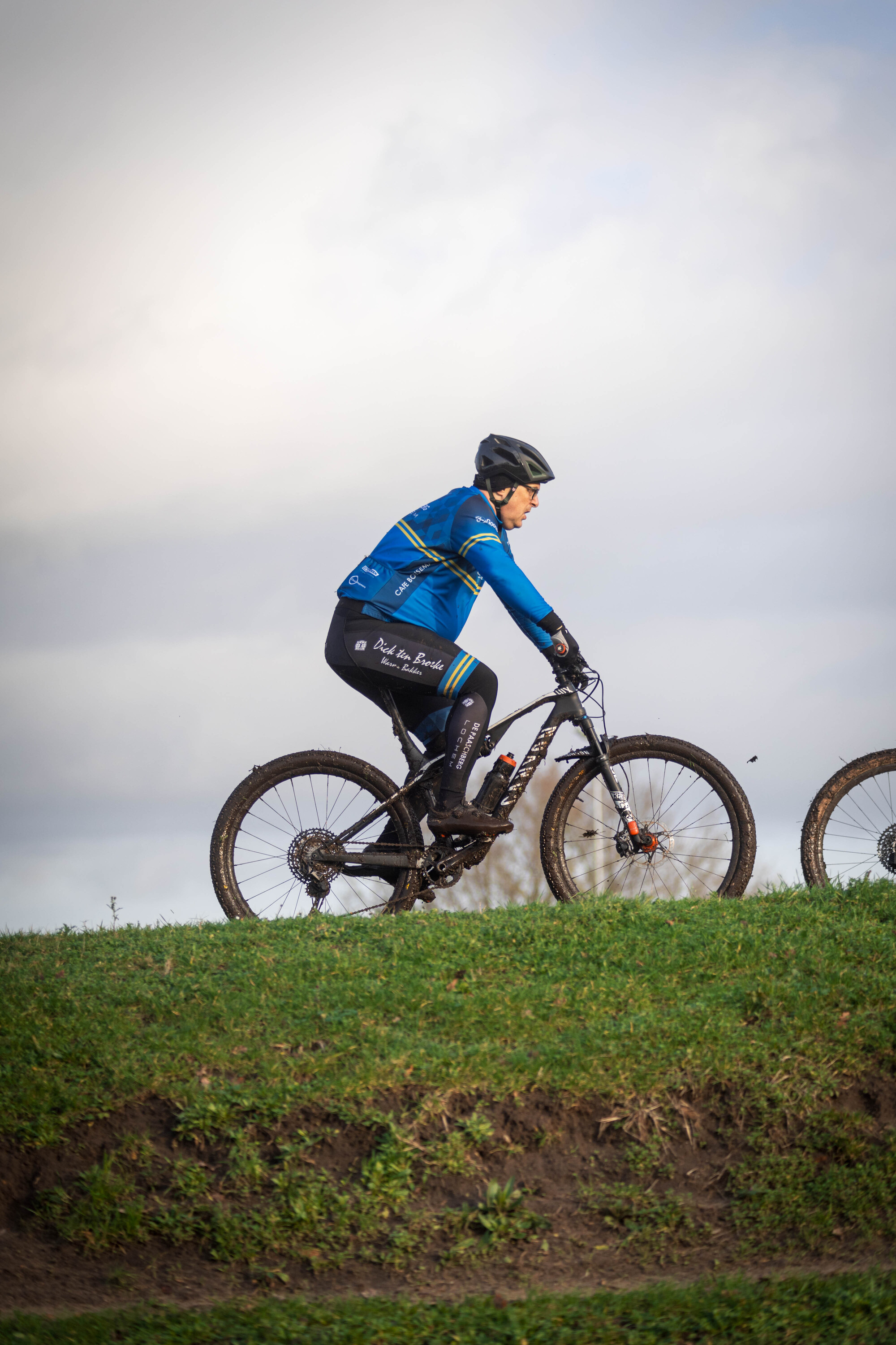 A man in a blue shirt is riding a bike through the grass, with another bike next to him.