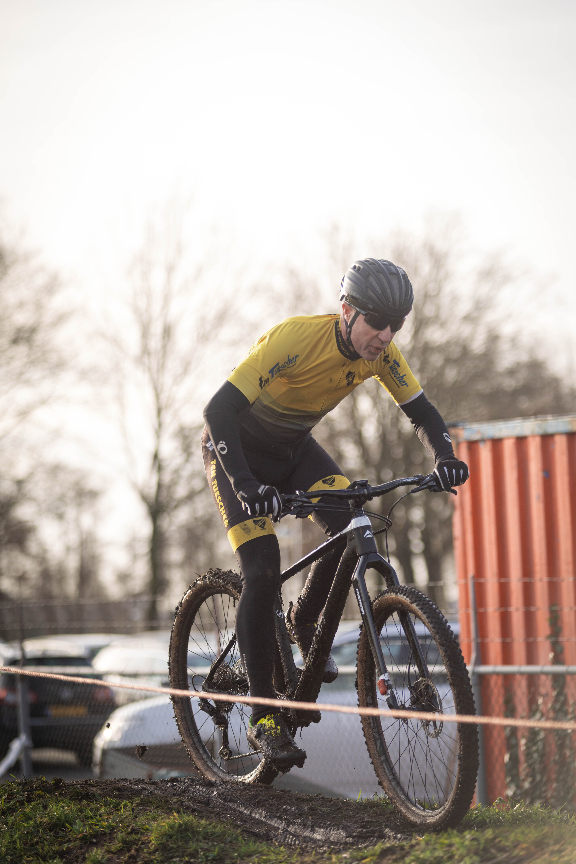 A young person on a bike in the mud wearing a yellow top and black pants.