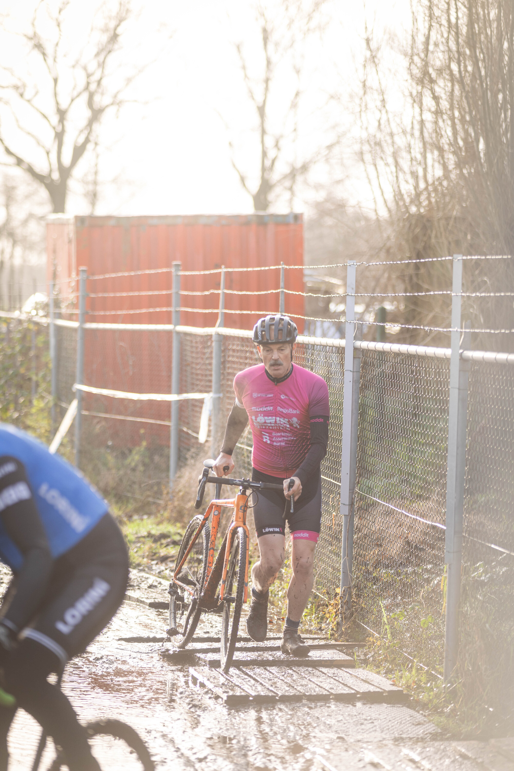 A man in a red and black shirt is riding a bike on a muddy track.