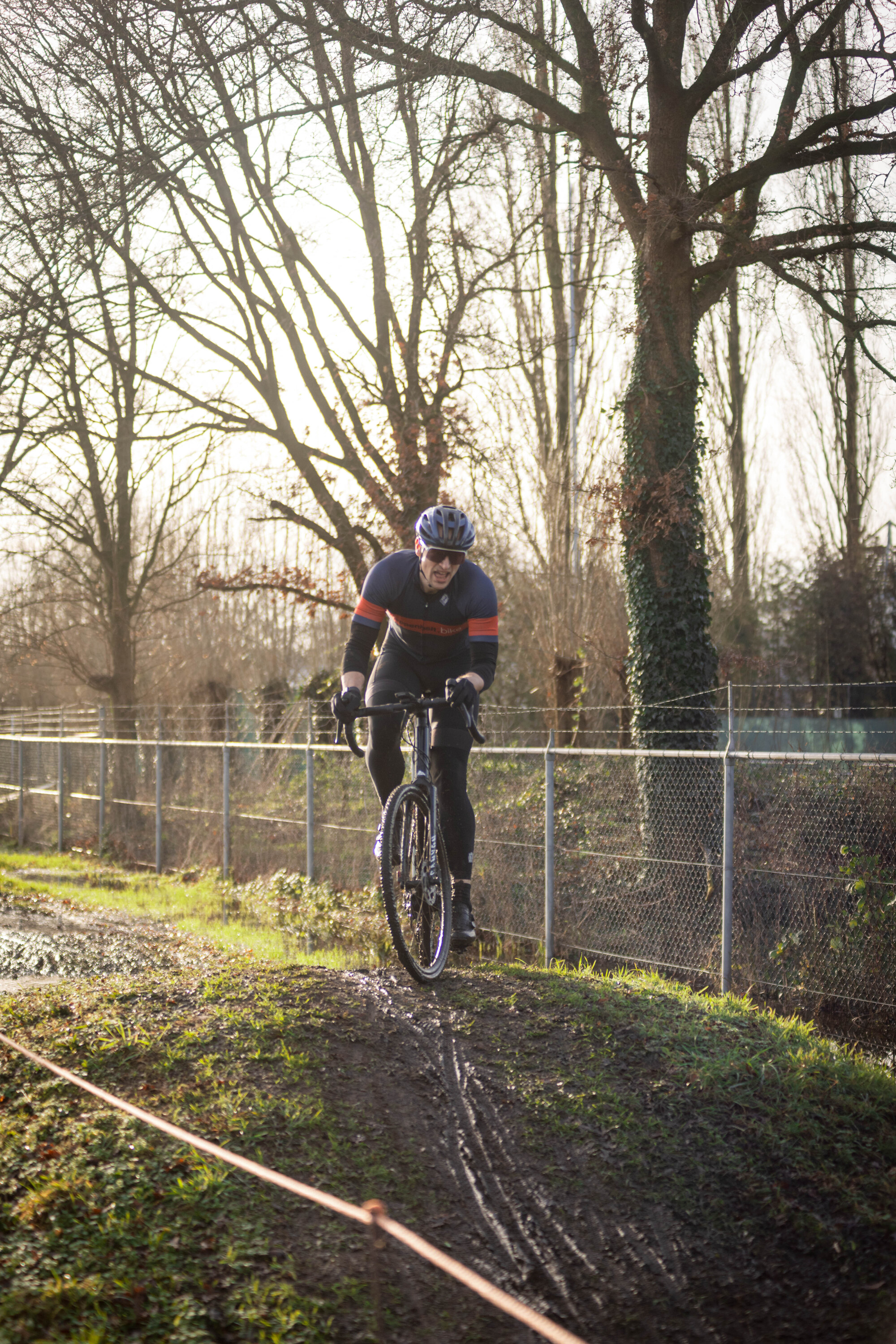 A man in a blue shirt and black pants is riding a black bike on dirt.