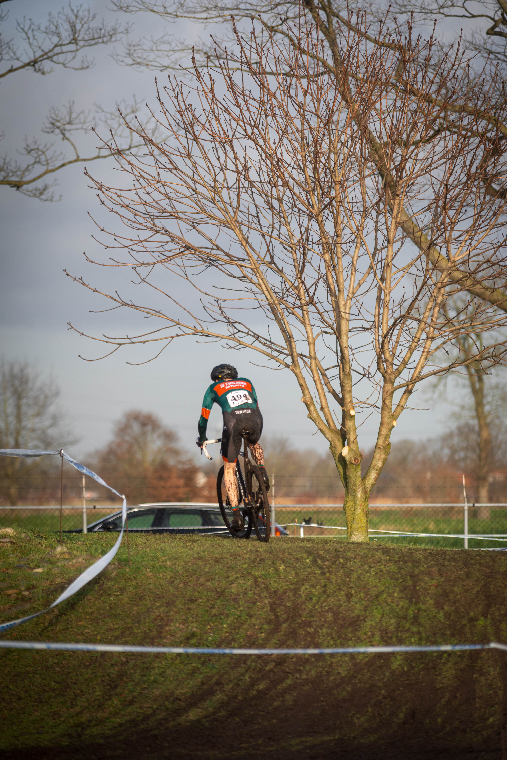 A man in a green jersey is wearing number 10 and riding a bicycle. He is near a tree on a hillside.