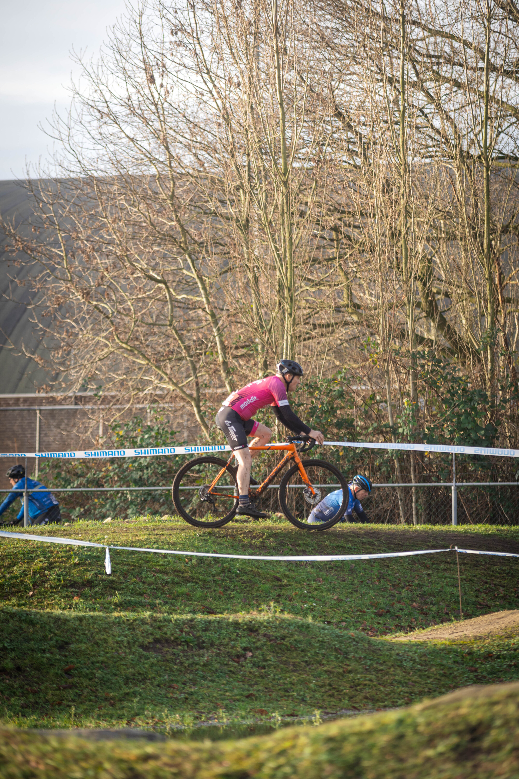 A person in a pink jersey is racing their bicycle through a course of jumps and obstacles.