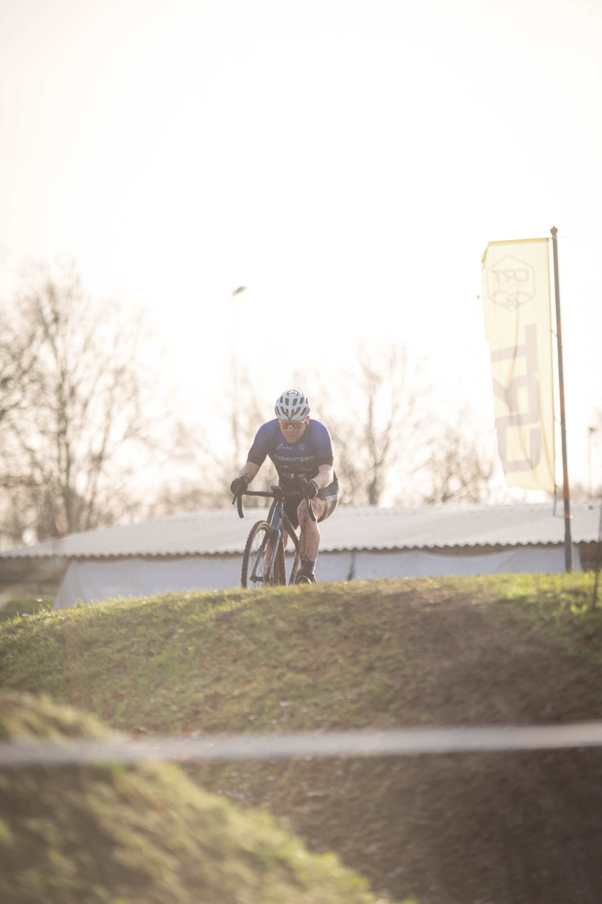 A man in a blue shirt and helmet is riding a bike up the side of a small hill at the Cyclocross Masters event.