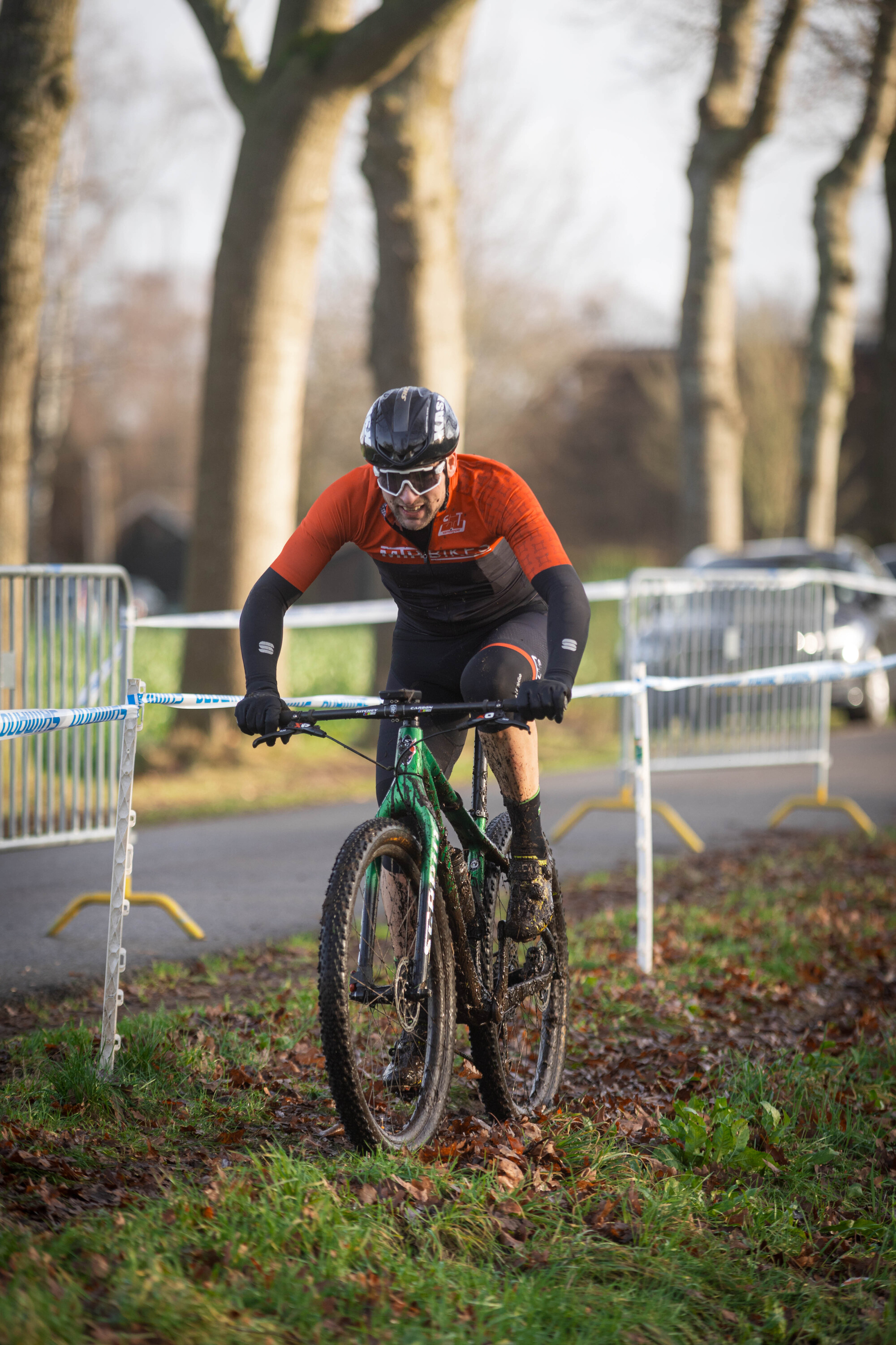 A man in a red and black shirt is riding his bicycle on an off road track.