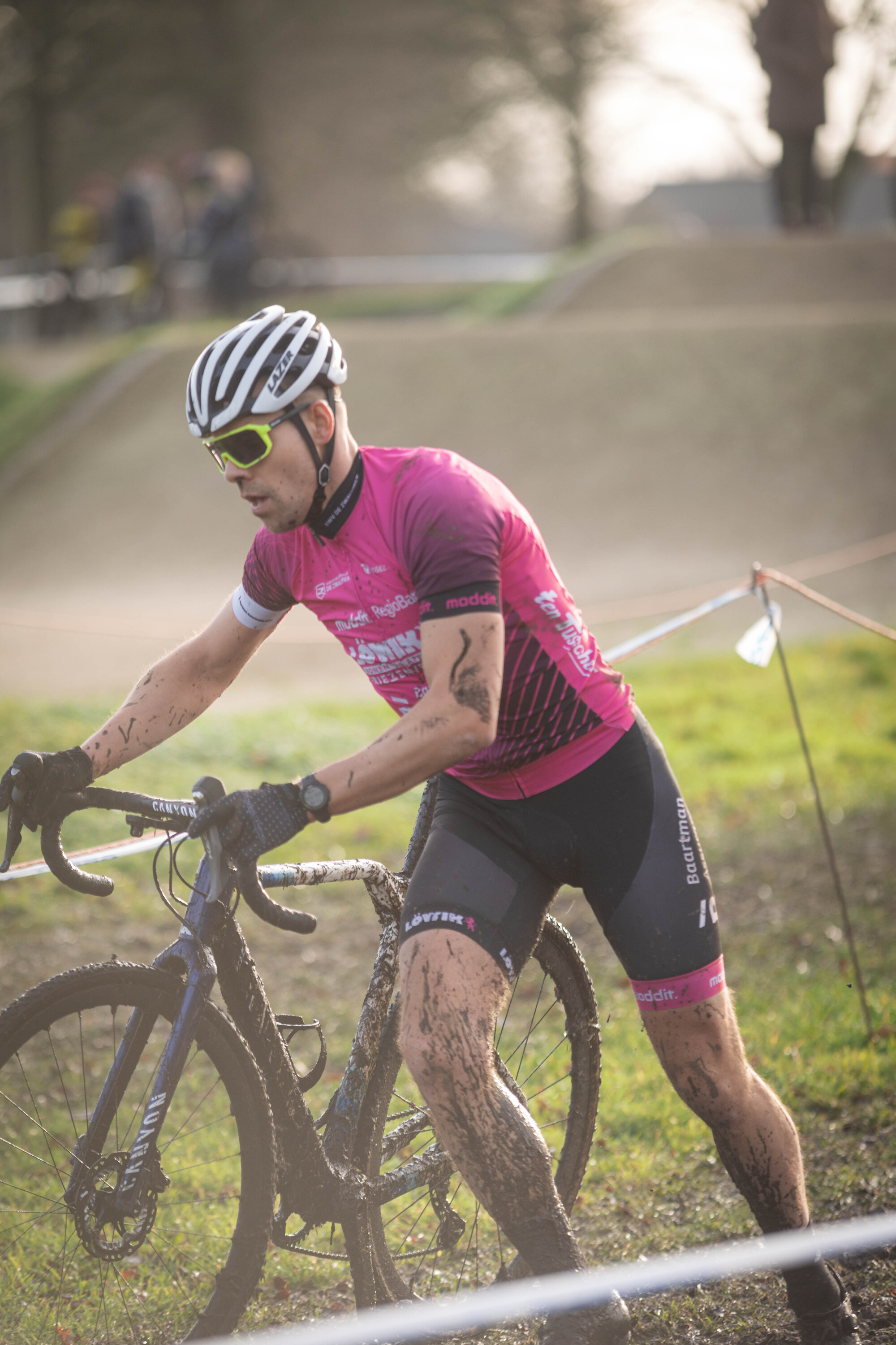 A man in a pink track suit riding a blue bicycle in the mud.