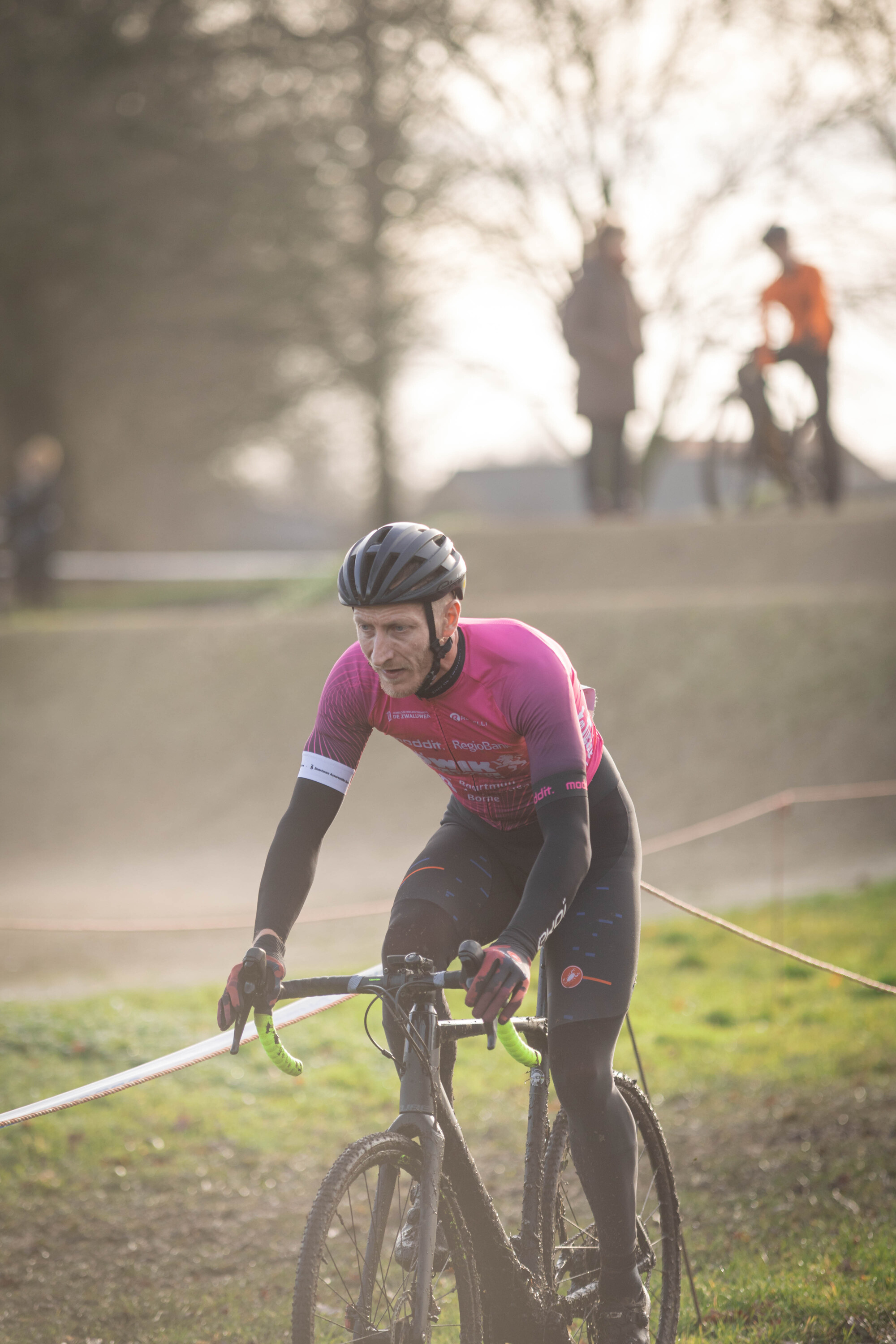 A man in a pink shirt is riding a bike on a race track at the Masters cyclocross event.