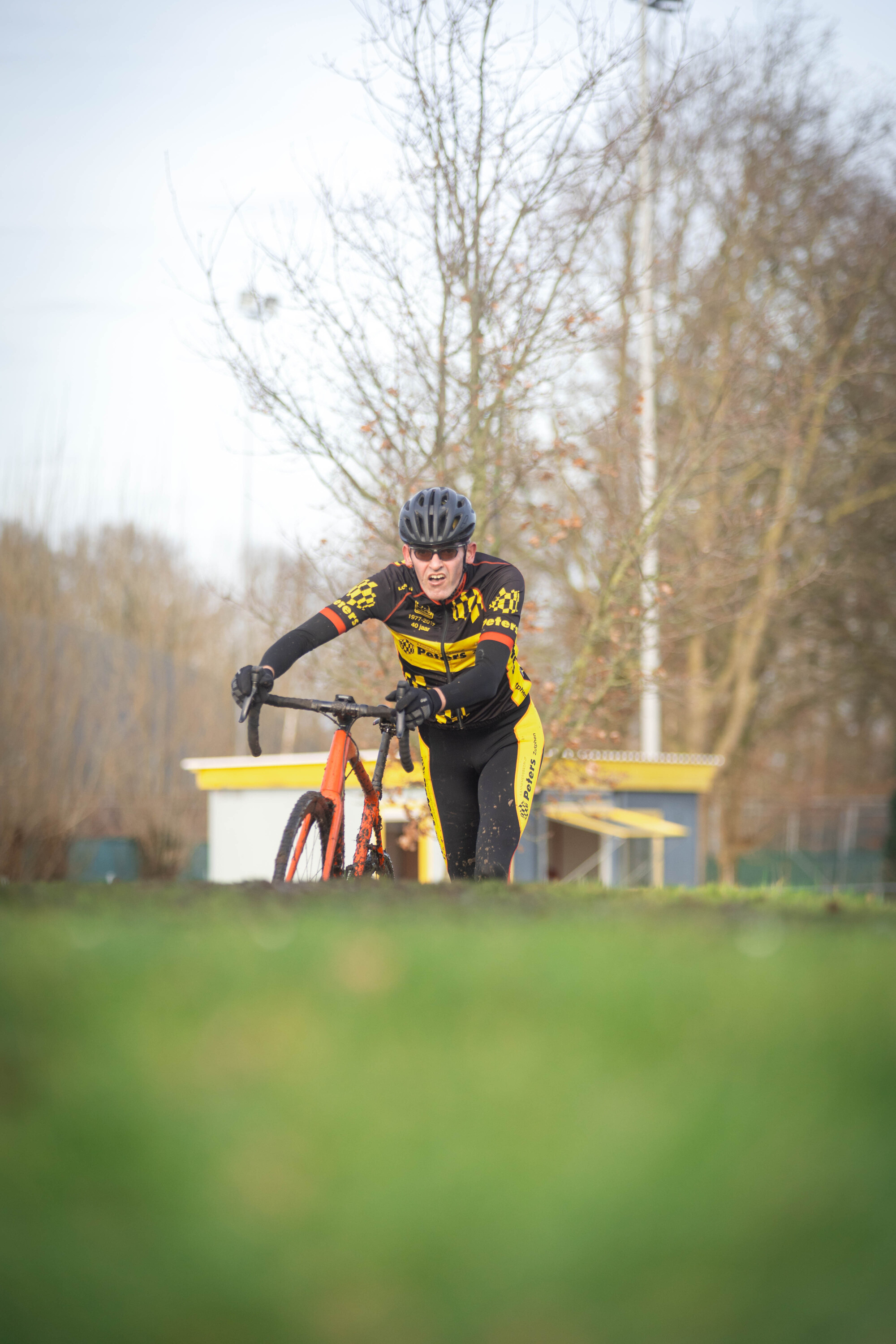 A person wearing a black helmet on top of a yellow and black bicycle in the grass.