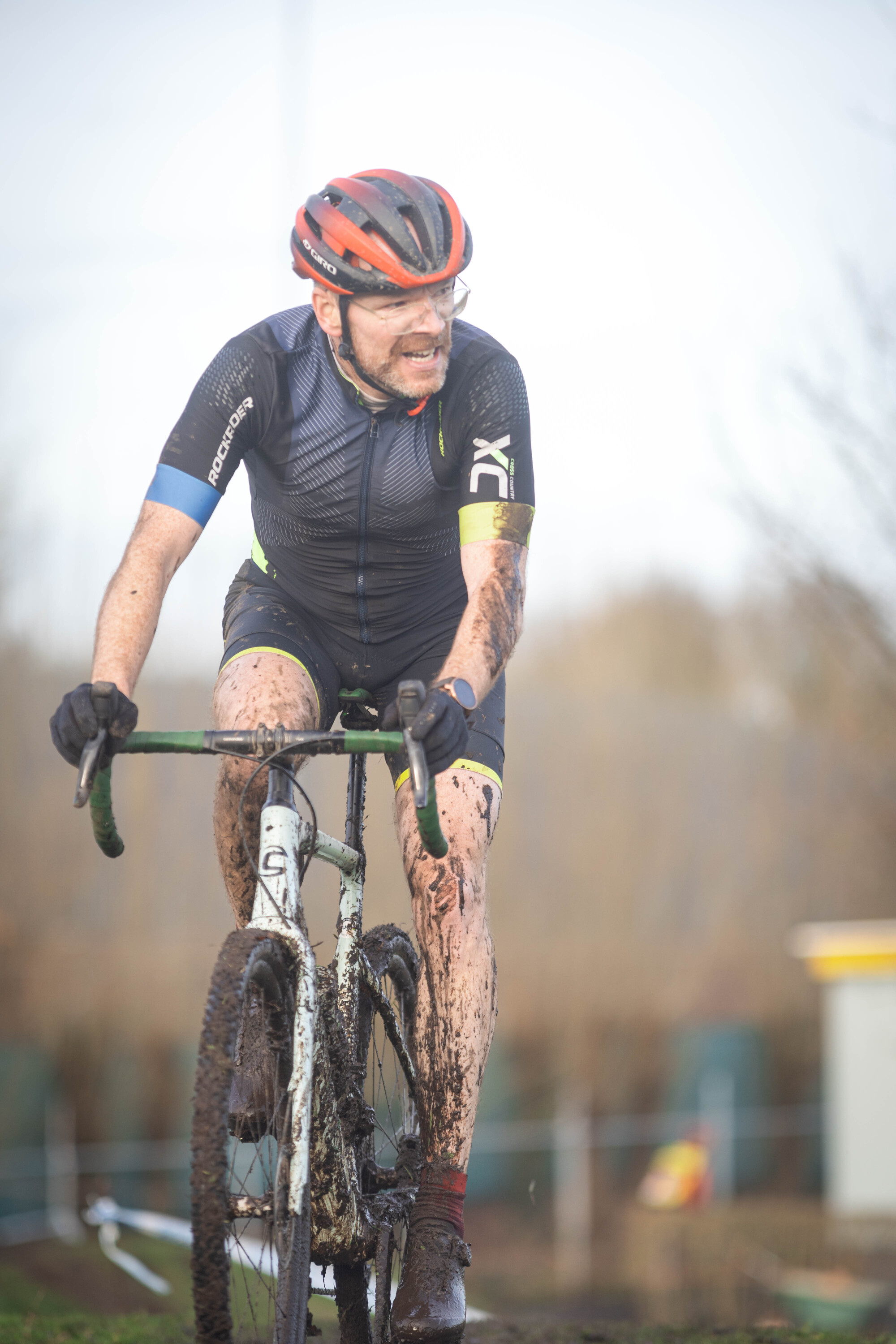 Man in a black and red outfit riding a muddy bike.