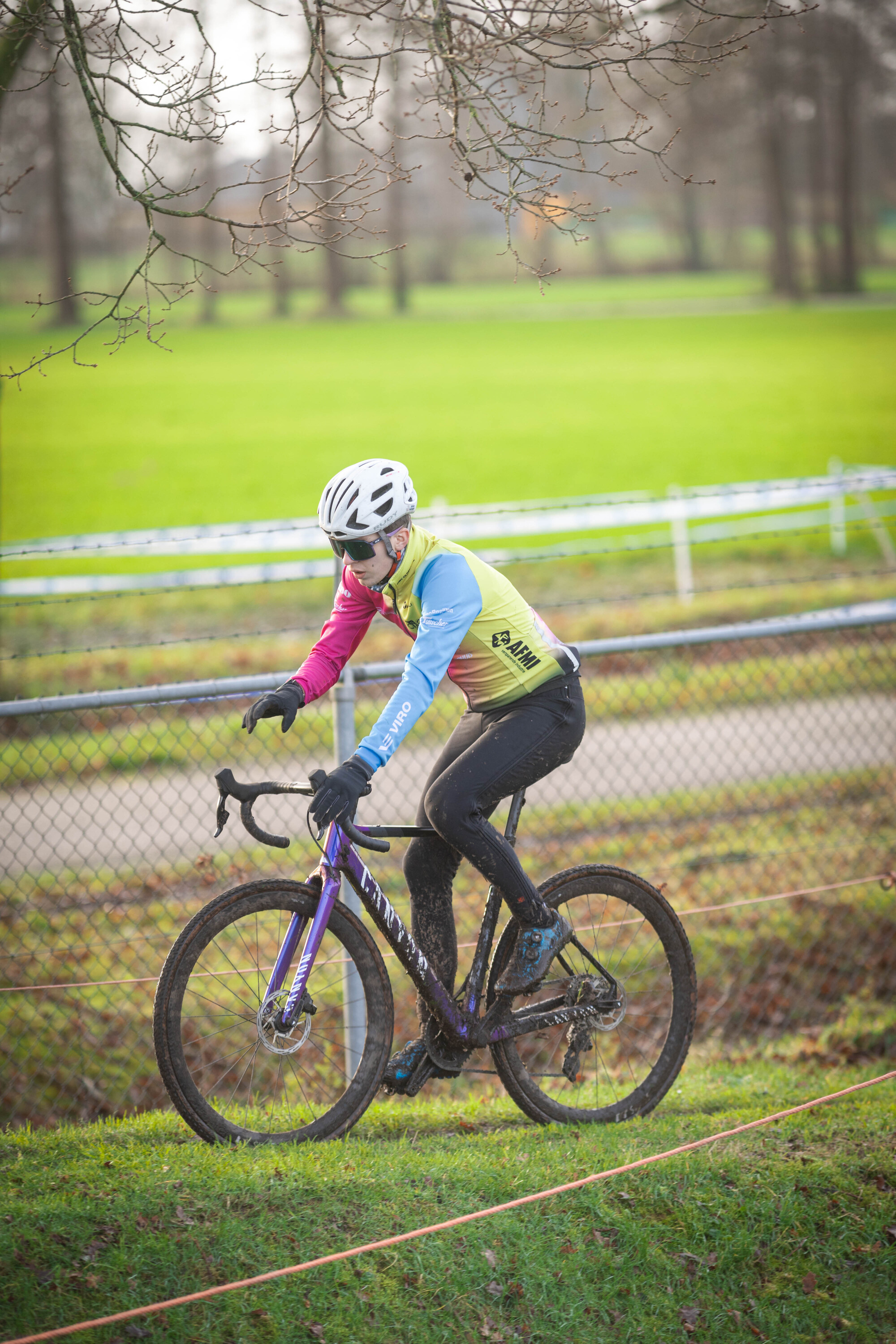 A cyclist in a blue and pink shirt riding a purple bicycle.