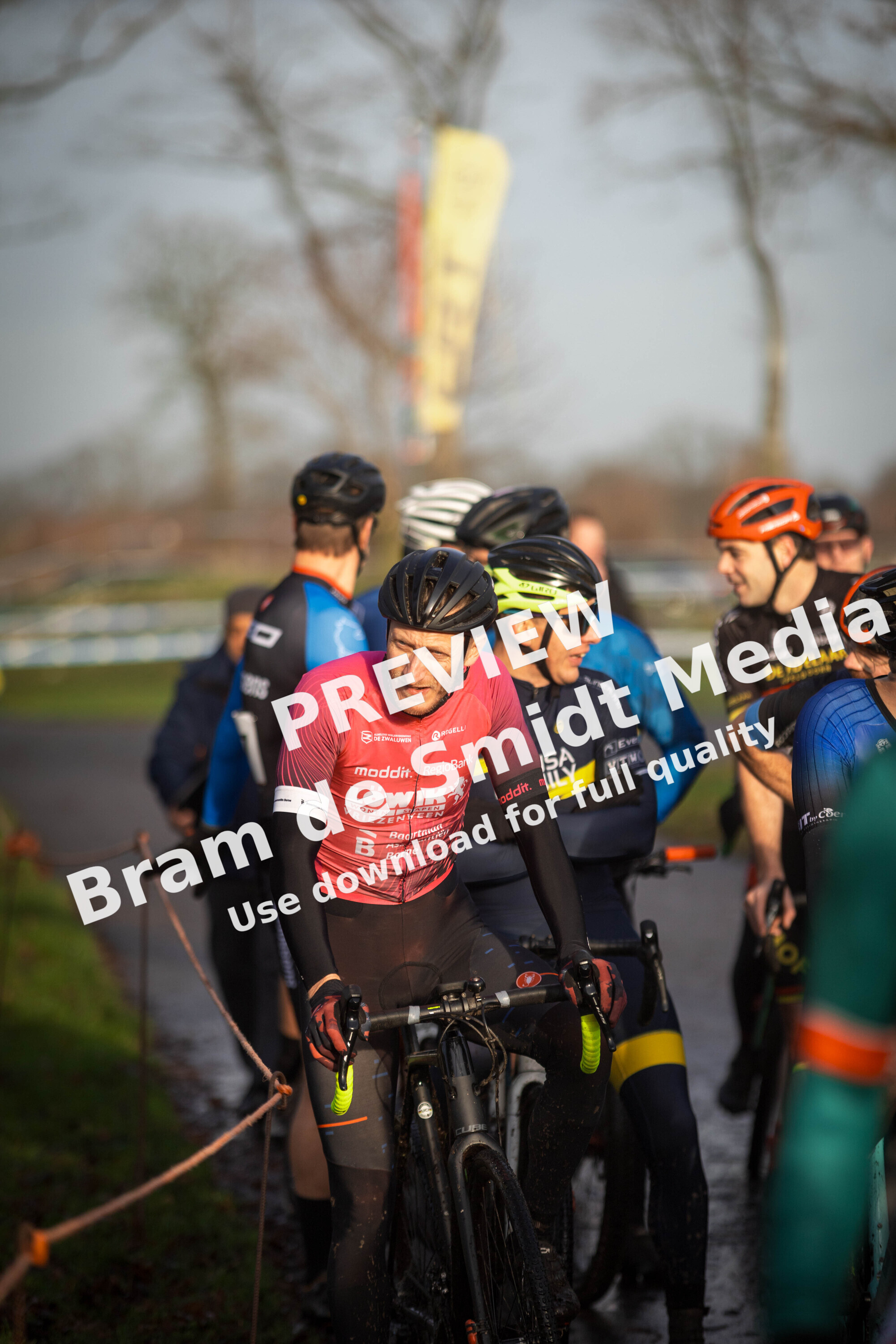 Several people with their bikes gathered in a grassy area, some wearing red and blue shirts.