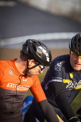 Two cyclists are in the middle of a race, wearing helmets and riding hard.