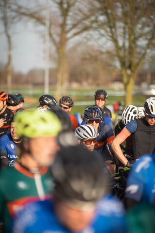 A group of cyclists are gathered for a cyclocross race. They are all wearing helmets and have their bikes with them.