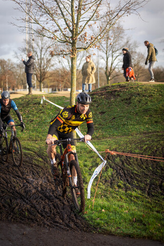 A man in a black, blue and yellow shirt rides his bike on a small hill.