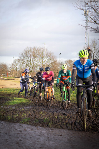 A man wearing a blue shirt with the word "Giant" on it rides his bike down a muddy track with several other cyclists.