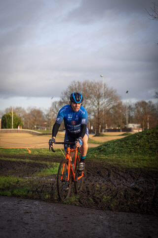 A man in a blue shirt is riding his bicycle on muddy ground.