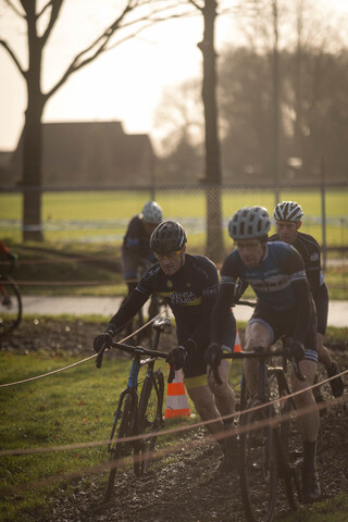 Cyclists wearing helmets and blue and black outfits on a grassy field.