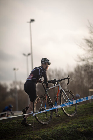 A man wearing a number 23 on his jersey is riding a black and orange bike at a cross country race.